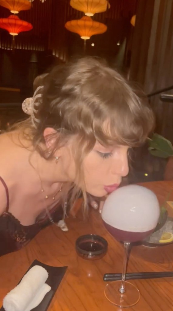 Taylor Swift blowing out a bubble on a drink.