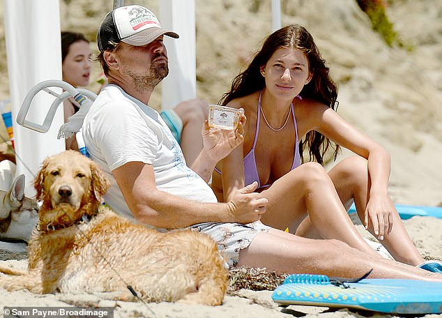 Picnic pals: DiCaprio enjoyed a snack, as his loyal golden retriever lied down next him, looking damp from swim